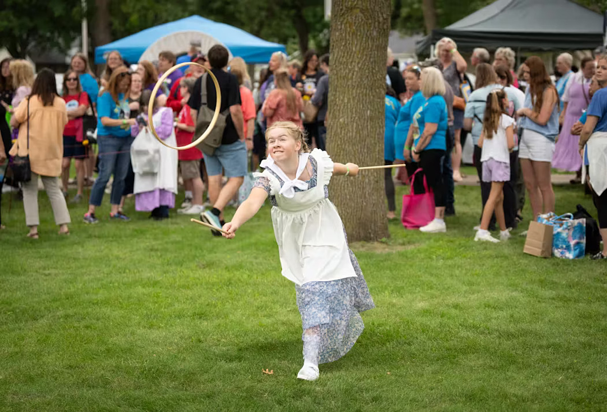 3amfptec6vf5xk2sszhje3ajc4-172-4321-5605-1721635456-1 Trong khi mẹ xếp hàng xin chữ ký của Dean Butler (vai Almanzo Wlider, chồng của Laura Ingalls Wilder), Danea Jackson, 12 tuổi, đến từ Wilton (bang Iowa), chơi trò graces (trò chơi phổ biến dành cho các cô gái trẻ vào đầu những năm 1800) ở lễ hội. Một người sẽ ném chiếc vòng gỗ lên không trung để người kia bắt lấy bằng hai thanh gỗ. Người chiến thắng là người đầu tiên bắt được chiếc vòng mười lần. Ảnh: StarTribune