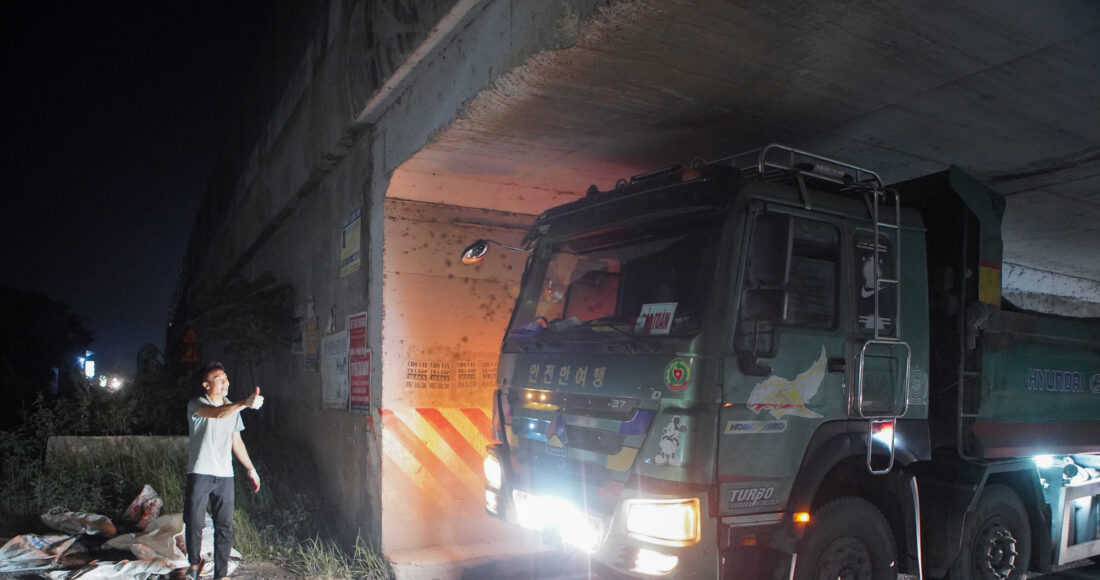 Điều phối viên hướng dẫn tài xế xe tải cán qua đoạn vừa rải nhựa đường để ép phẳng, tối 17/5. Ảnh: Quỳnh Nguyễn