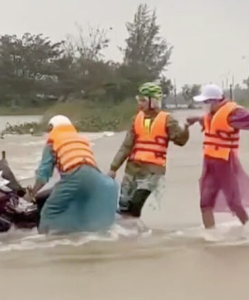 Một người dân đi qua đoạn đường thôn Đông Bình, xã Duy Vinh, huyện Duy Xuyên bị nước cuốn xe máy được nhiều người hợp sức kéo lên chiều 14/12. Ảnh: Nguyễn Nở