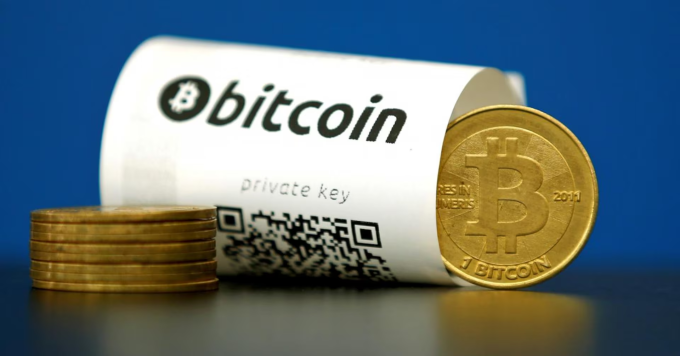 Biểu trưng của Bitcoin đặt cạnh một biên lai có chứa mã QR truy cập vào ví lưu trữ. Ảnh: Reuters